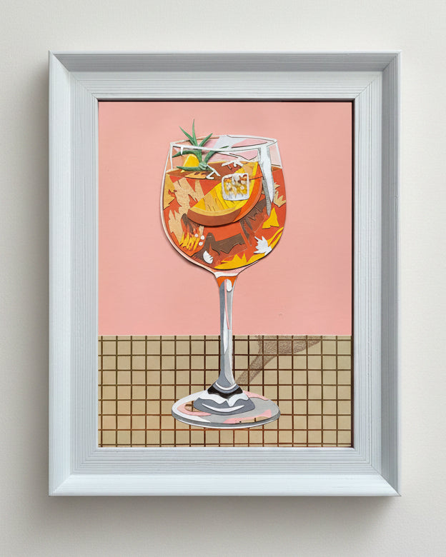 Framed artwork of an Aperol Spritz on a pink background and checkered tablecloth.