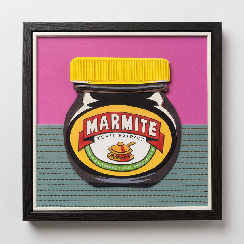 A framed art print featuring a stylized illustration of a Marmite Yeast Extract jar, set against a split pink and grey background, 