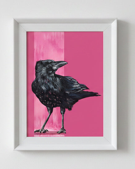 A framed art print featuring a detailed black raven against a vibrant pink background, housed in a white frame.
